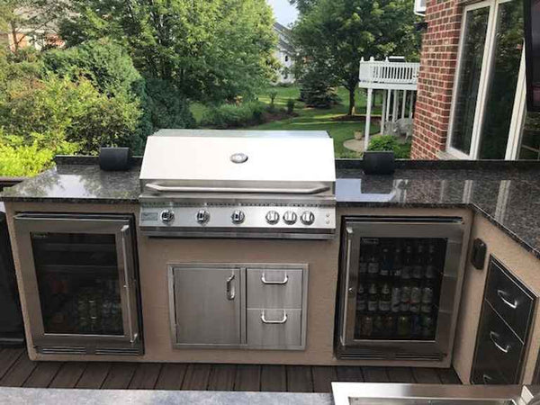 KoKoMo grill installed in an outdoor kitchen island with dark countertops, cabinets and glass-door appliances