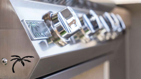 Angled close-up of the KoKoMo grill badge, polished control knobs and palm-tree cutout