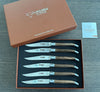 Six Laguiole en Aubrac walnut steak knives in an open brown gift box with its branded lid and information booklet alongside