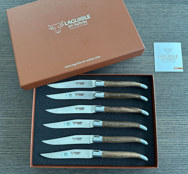 Six Laguiole en Aubrac walnut steak knives in an open brown gift box with its branded lid and information booklet alongside