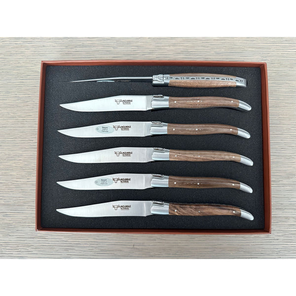 Overhead view of six walnut-handled steak knives in a fitted brown presentation box, with one knife turned to show its decorative spine