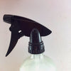 Clear spray bottle with black nozzle on a light pink background