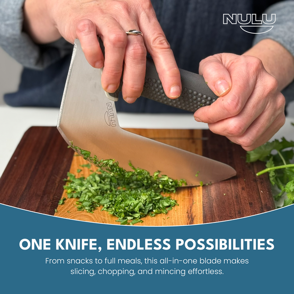 Two hands rocking the NULU curved kitchen knife over chopped herbs on a wooden cutting board