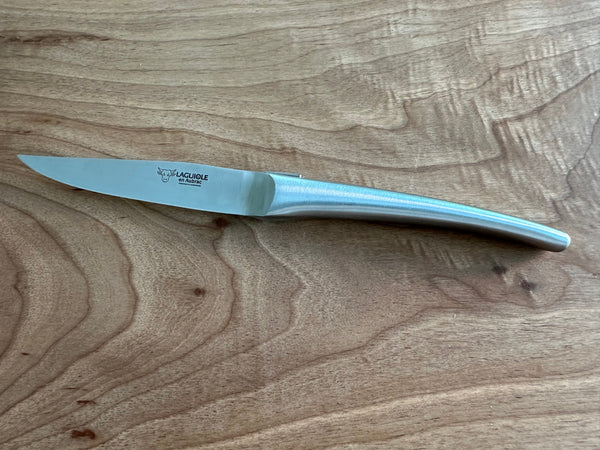 Side view of a Laguiole en Aubrac steak knife with a branded blade and curved matte stainless steel handle