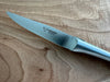 Close-up of the Laguiole en Aubrac logo on a steak knife blade beside its matte stainless steel handle