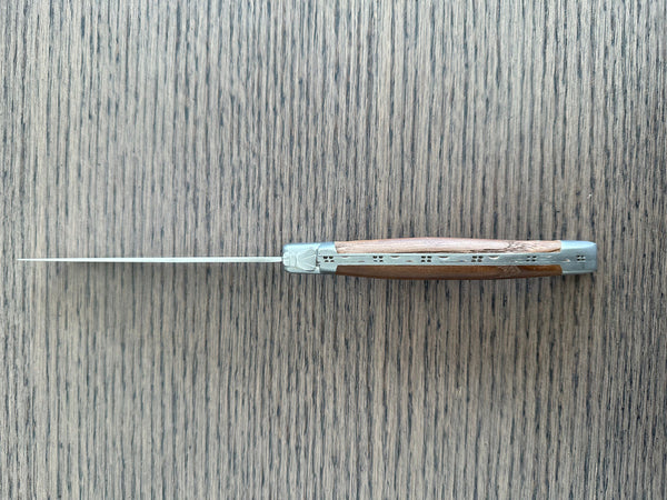 Top view of a single Laguiole en Aubrac ash wood steak knife showing its decorative spine on a gray wood surface