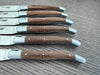 Close-up of six ash wood steak knife handles showing variations in wood grain and Shepherd’s Cross detailing