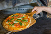 Bamboo pizza peel sliding a fresh artisanal pizza into the oven, heat-resistant wooden kitchen tool