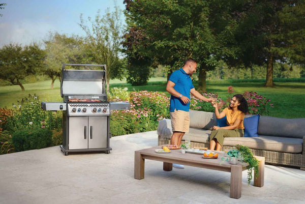 “Two people enjoying a garden patio beside an open Napoleon Rogue PRO-S 525 grill.”