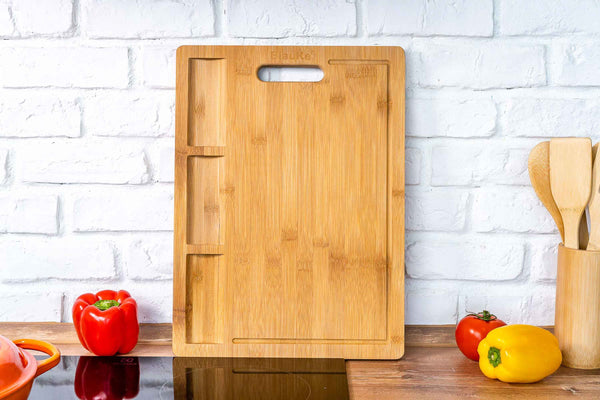 Wooden cutting board on a kitchen counter with vegetables and utensils.