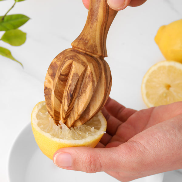 Handheld wooden citrus juicer pressing a fresh lemon into a glass, eco-friendly bartending and cooking accessory