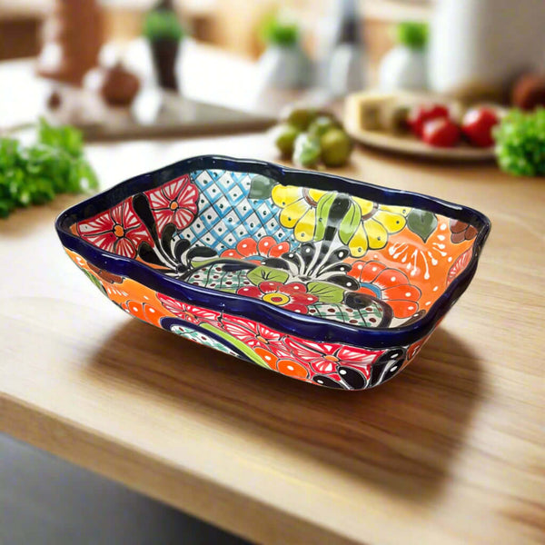 Angled view of a rectangular Talavera serving dish with colorful floral patterns and a dark blue rim on a wooden kitchen counter