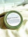 Candle jar lid with 'Abundance Candle label on a beige fabric background