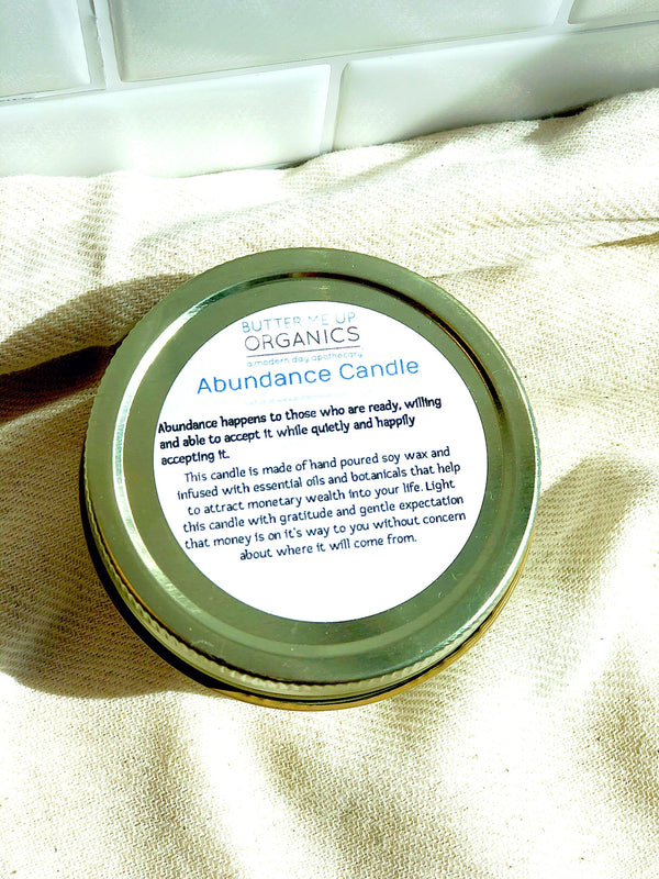 Candle jar lid with 'Abundance Candle label on a beige fabric background