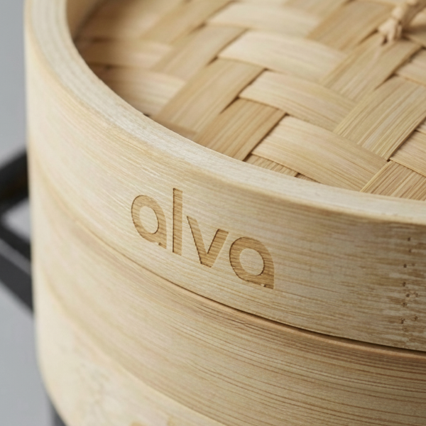 Close-up of the Alva logo engraved on a bamboo steamer basket, showing its slatted base and natural grain