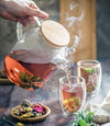 Thermo Glass Teapot filled with blooming herbal tea on a wooden tray