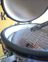 Tongs lifting the hinged cooking grate above glowing charcoal inside an open KoKoMo Kamado grill