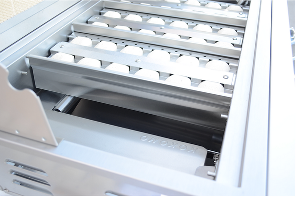 KoKoMo grill interior showing rows of pale briquettes in metal trays above the burners