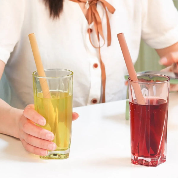 Two glasses with straws, one containing a yellow liquid and the other a red liquid, on a white surface.
