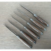 Six walnut-handled knives arranged diagonally on gray wood, showing decorative metal spines and bee emblems