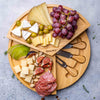 Wooden charcuterie board with cheeses, fruits, and meats, featuring Blauke branding.