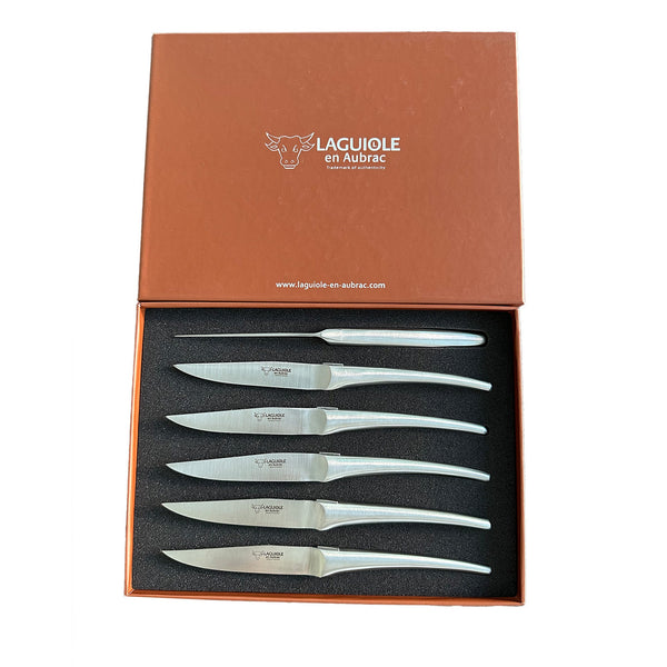 Six Laguiole en Aubrac matte stainless steel steak knives arranged in an open brown presentation box with a black fitted insert