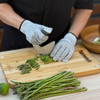 Person wearing gray NULU cut-resistant gloves while chopping asparagus with a curved knife on a wooden cutting board
