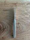 Top view of a single Laguiole en Aubrac steak knife showing its slim blade profile and matte stainless steel handle on wood