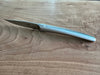 Angled view of a Laguiole en Aubrac steak knife showing its curved matte steel handle and blade on a wooden surface