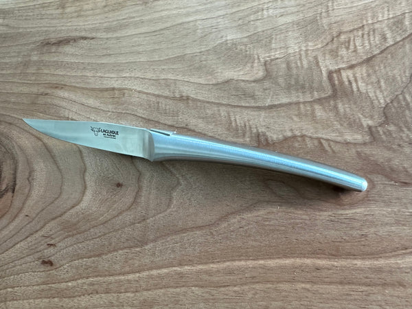Laguiole en Aubrac matte steel steak knife resting diagonally on wood, showing the blade and tapered handle