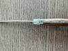 Close-up of the bee emblem and patterned metal spine where the blade meets the ash wood handle