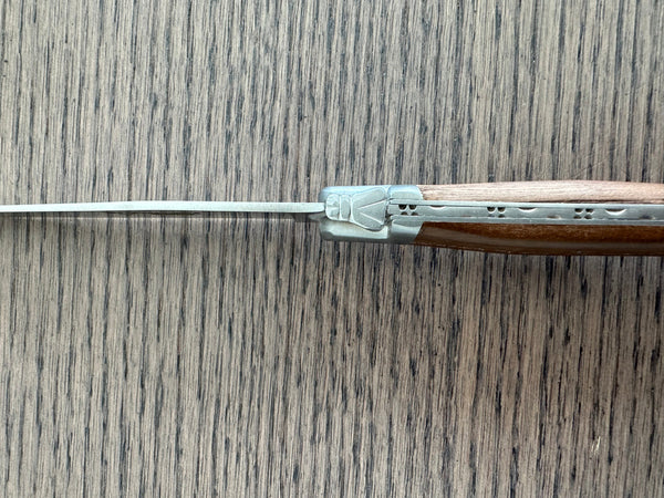 Close-up of the bee emblem and patterned metal spine where the blade meets the ash wood handle