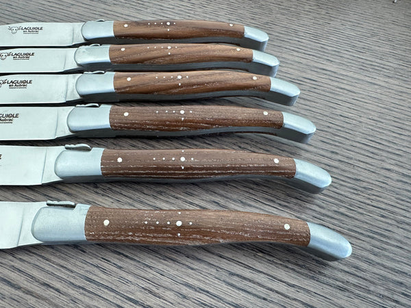 Close-up of six ash wood steak knife handles showing variations in wood grain and Shepherd’s Cross detailing