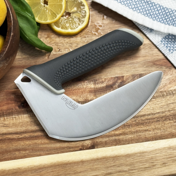 NULU kitchen knife resting on a wooden cutting board beside lemon slices, basil and a patterned kitchen towel