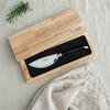 Ebony-handled pizza knife in a wooden presentation box on light fabric beside rosemary and a fringed napkin