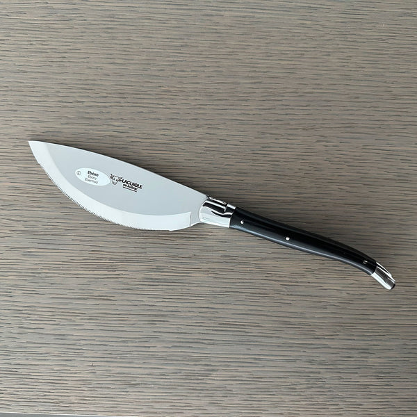 Laguiole en Aubrac serrated pizza knife with an ebony wood label on the blade, resting on a gray wooden surface
