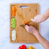 Person chopping vegetables on a wooden cutting board with compartments, branded 'Blauke'.