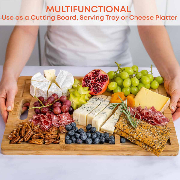 Wooden cutting board with assorted fruits, cheeses, and meats on a white background.
