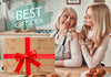 Two women in a kitchen with a wooden cutting board wrapped in a red ribbon, labeled 'Best Gift Idea'.