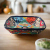Front view of a rectangular Talavera serving dish with blue, green and red floral patterns on a wooden counter