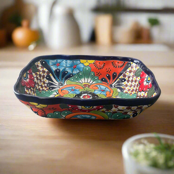 Front view of a rectangular Talavera serving dish with blue, green and red floral patterns on a wooden counter